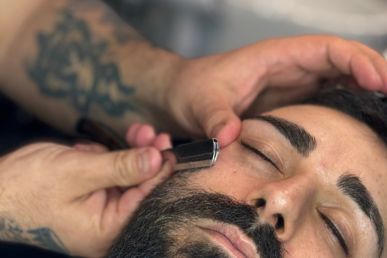 Una persona con gli occhi chiusi si rilassa mentre il barbiere gli rasa la barba