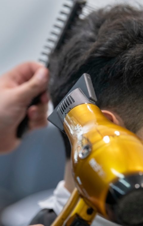 Una persona riceve un taglio di capelli usando un tagliacapelli elettrico, con una mano esperta che tiene un pettine per guidare il processo. Il tagliacapelli giallo è al centro della scena mentre taglia abilmente i capelli nella parte posteriore della testa, proprio come li troveresti da un parrucchiere a Fiumefreddo di Sicilia.